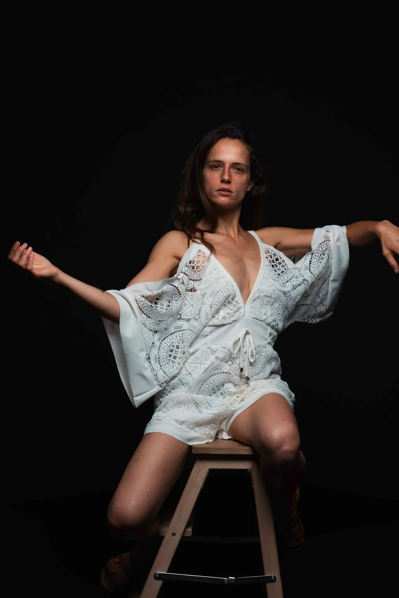 Studio portrait — model on stool, lace dress on black.